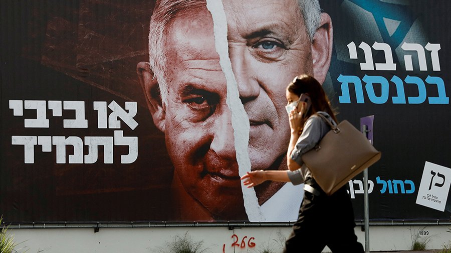 A woman walks past a Blue and White party election campaign banner depicting its leader, Israeli Defence Minister Benny Gantz, alongside Israeli Prime Minister Benjamin Netanyahu in Tel Aviv, Israel March 14, 2021. REUTERS/Corinna Kern/File Photo